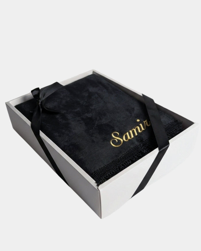 Tapis de prière en velours noir avec le prénom Samir brodé en fil doré, présenté dans un coffret cadeau blanc noué d'un ruban noir assorti