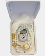 Gros plan du tasbih en perles blanches, compteur digital serti de strass et de fleurs, fermoirs dores et pompon en soie blanche